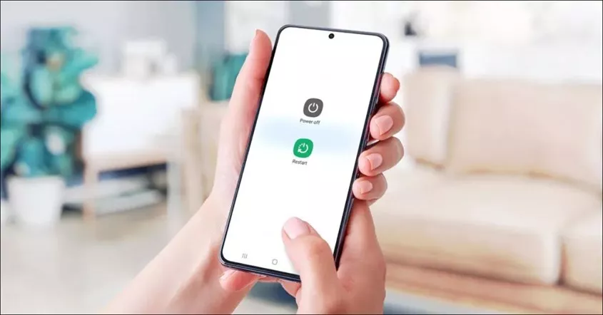 Tangan memegang HP RAM 12 GB yang menampilkan menu restart dan power off pada layar.