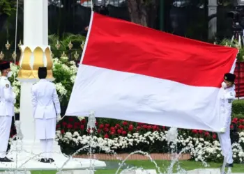 Tiga anggota Paskibraka membentangkan bendera Merah Putih raksasa di tiang bendera Istana Negara.