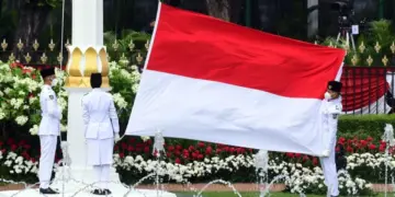Tiga anggota Paskibraka membentangkan bendera Merah Putih raksasa di tiang bendera Istana Negara.