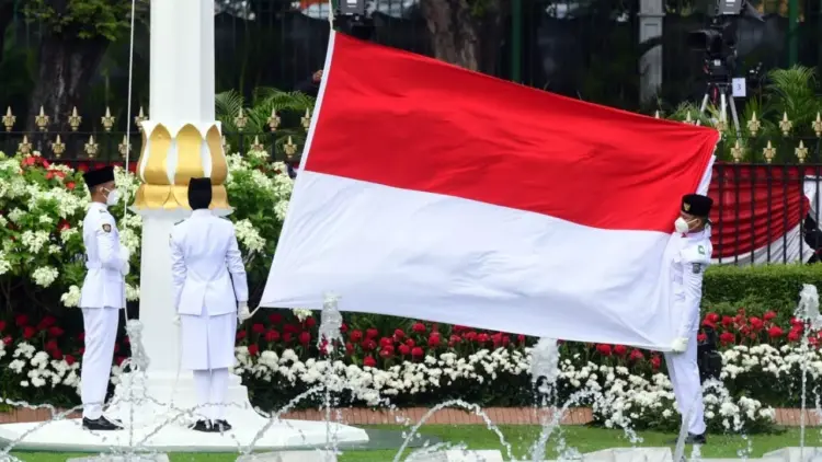 Tiga anggota Paskibraka membentangkan bendera Merah Putih raksasa di tiang bendera Istana Negara.