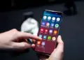 Tangan memegang smartphone Android sambil menyentuh menu pengaturan pada layar.
