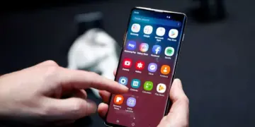 Tangan memegang smartphone Android sambil menyentuh menu pengaturan pada layar.