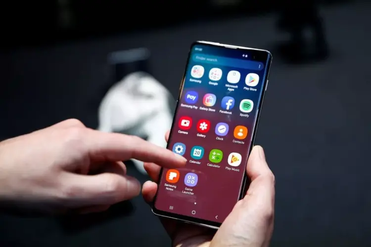 Tangan memegang smartphone Android sambil menyentuh menu pengaturan pada layar.
