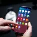 Tangan memegang smartphone Android sambil menyentuh menu pengaturan pada layar.