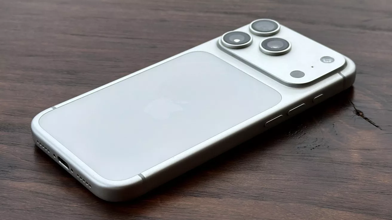 iPhone perak tergeletak miring di atas meja kayu memperlihatkan susunan tiga lensa Kamera iPhone 18 Pro Max secara detail.