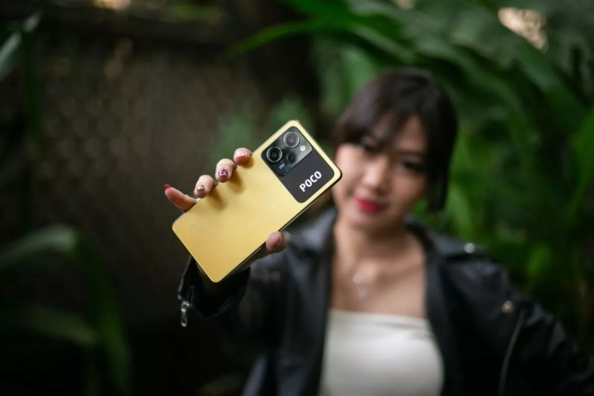 Seorang wanita memegang HP POCO berwarna kuning dengan modul kamera hitam yang elegan.