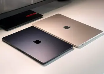 Dua unit MacBook Air tertutup warna Midnight dan Starlight berdampingan di atas meja putih.