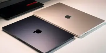 Dua unit MacBook Air tertutup warna Midnight dan Starlight berdampingan di atas meja putih.