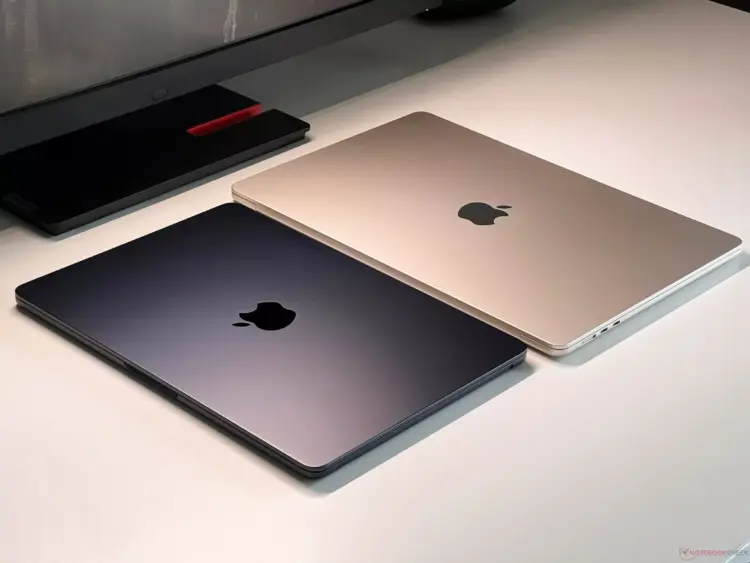 Dua unit MacBook Air tertutup warna Midnight dan Starlight berdampingan di atas meja putih.