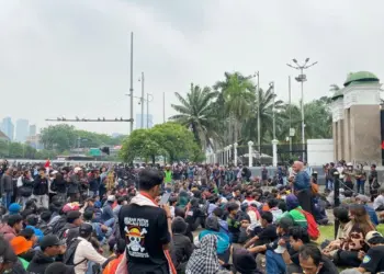 Peserta demo Jakarta duduk tertib di sekitar jalanan dekat gerbang gedung DPR RI.