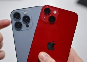 Tangan memegang iPhone varian Pro warna abu-abu dan varian standar warna merah (PRODUCT RED).