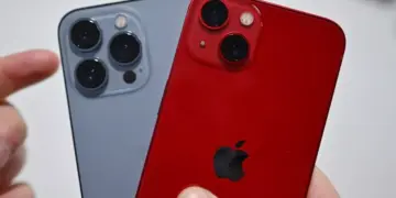 Tangan memegang iPhone varian Pro warna abu-abu dan varian standar warna merah (PRODUCT RED).