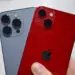 Tangan memegang iPhone varian Pro warna abu-abu dan varian standar warna merah (PRODUCT RED).