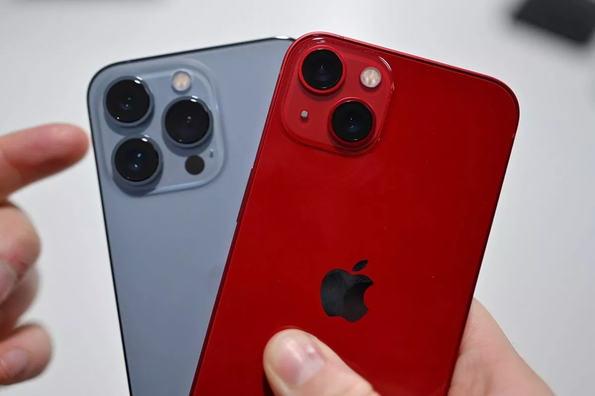 Tangan memegang iPhone varian Pro warna abu-abu dan varian standar warna merah (PRODUCT RED).