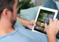 Seseorang sedang santai di sofa menggunakan tablet layar lebar ber-SIM card untuk menonton film.