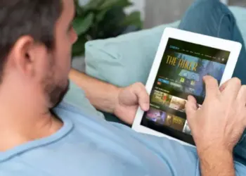 Seseorang sedang santai di sofa menggunakan tablet layar lebar ber-SIM card untuk menonton film.