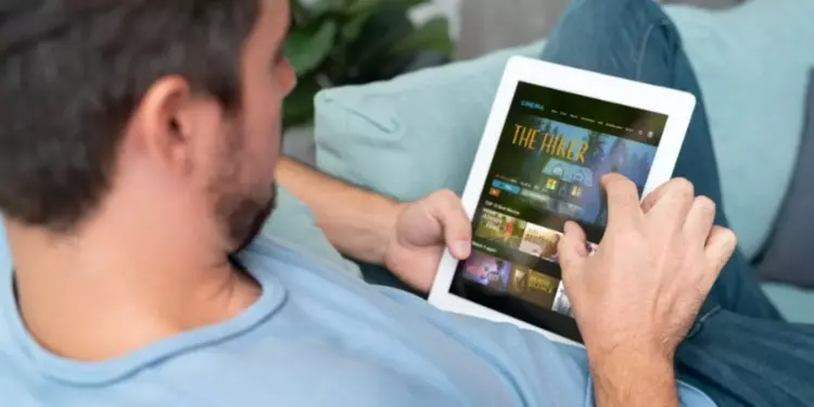 Seseorang sedang santai di sofa menggunakan tablet layar lebar ber-SIM card untuk menonton film.