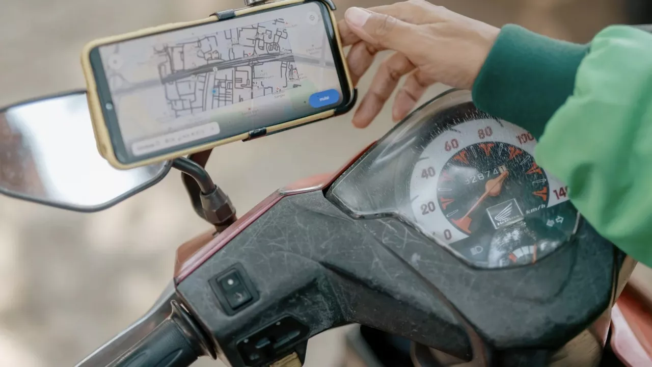 Pengemudi ojek online menggunakan smartphone yang terpasang di stang motor untuk melihat peta GPS navigasi HP untuk Ojol.