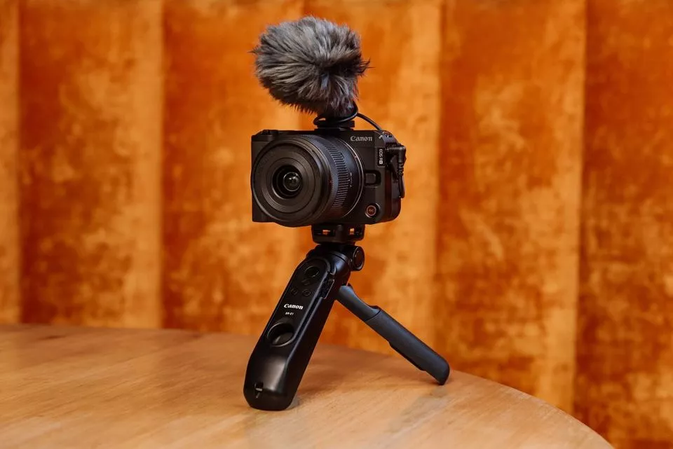 Canon EOS R50 V dengan windmuff mikrofon terpasang pada tripod meja kayu