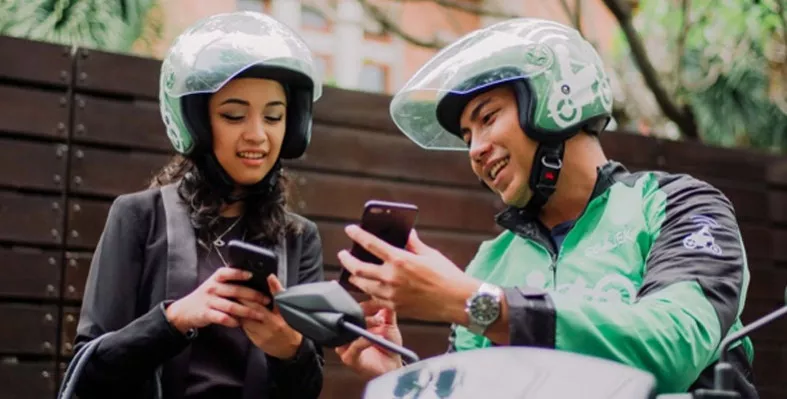 Driver ojek online berhelm hijau bersama penumpang sedang memegang smartphone untuk koordinasi titik jemput HP untuk Ojol.