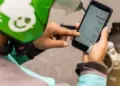 Tangan driver ojol mengenakan helm hijau sedang menekan layar smartphone yang menampilkan daftar aplikasi HP untuk Ojol.
