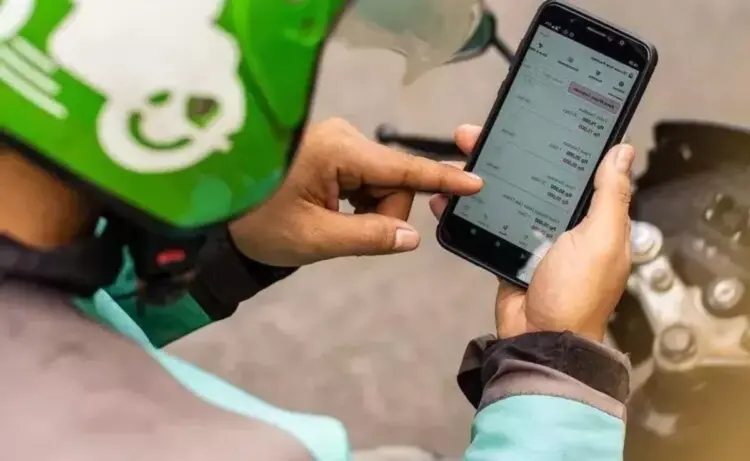 Tangan driver ojol mengenakan helm hijau sedang menekan layar smartphone yang menampilkan daftar aplikasi HP untuk Ojol.