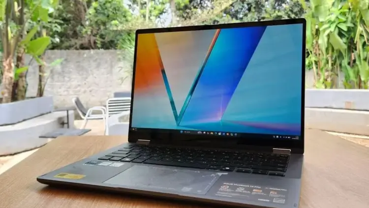 Laptop ASUS Vivobook 14 Flip TP3407AA terbuka di atas meja kayu dengan layar OLED berwarna cerah.