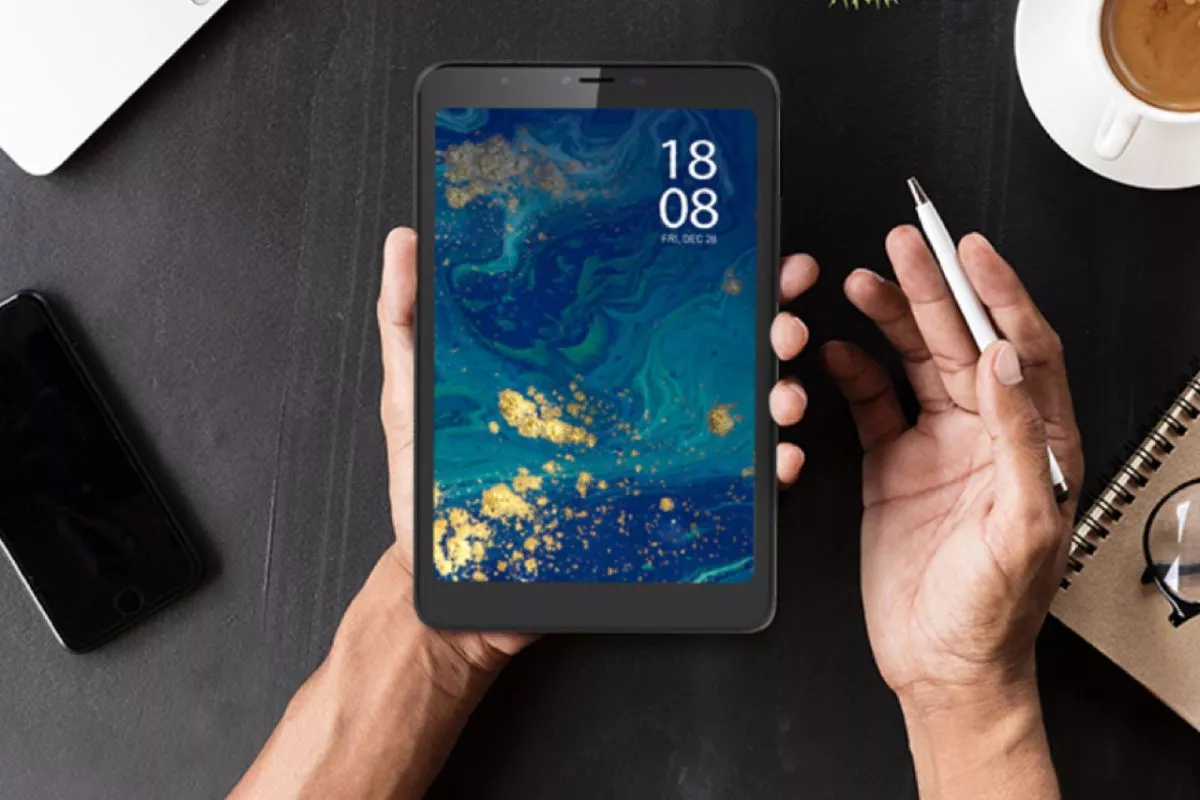 Seseorang memegang tablet Android 8 inci layar sentuh di atas meja kerja yang dilengkapi pena digital dan buku catatan.