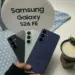 Seseorang memegang tiga varian warna Samsung Galaxy S26 FE di depan stand bertuliskan "Samsung Galaxy S26 FE".