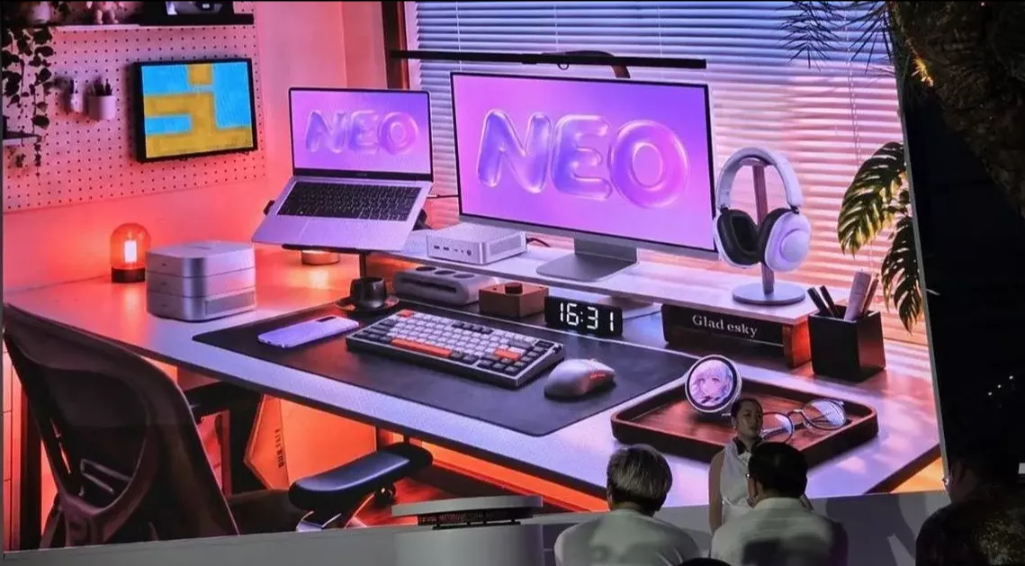 Setup meja kerja modern dengan monitor bertuliskan NEO, laptop, keyboard mekanikal, dan perangkat Infinix AI NAS serta Mini PC X1.
