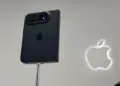 Penampakan bodi belakang iPhone Duo warna hitam terpasang pada stand pameran dengan logo Apple menyala di latar belakang.