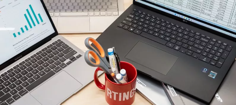 Beberapa laptop menampilkan grafik dan data keuangan di atas meja kerja untuk panduan spesifikasi laptop pebisnis.