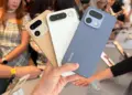 Seseorang memegang tiga unit HP Realme kamera 200MP dengan opsi warna emas, putih, dan biru di sebuah pameran gadget.