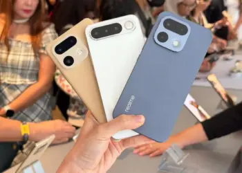Seseorang memegang tiga unit HP Realme kamera 200MP dengan opsi warna emas, putih, dan biru di sebuah pameran gadget.