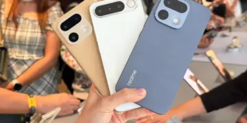 Seseorang memegang tiga unit HP Realme kamera 200MP dengan opsi warna emas, putih, dan biru di sebuah pameran gadget.