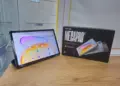 Wujud asli unit Tecno Megapad SE 2 menyala di samping kotak kemasan resminya di atas meja kayu.
