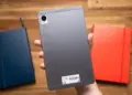 Sisi belakang tablet realme Pad Mini warna abu-abu yang digenggam satu tangan di atas meja kayu.