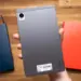 Sisi belakang tablet realme Pad Mini warna abu-abu yang digenggam satu tangan di atas meja kayu.