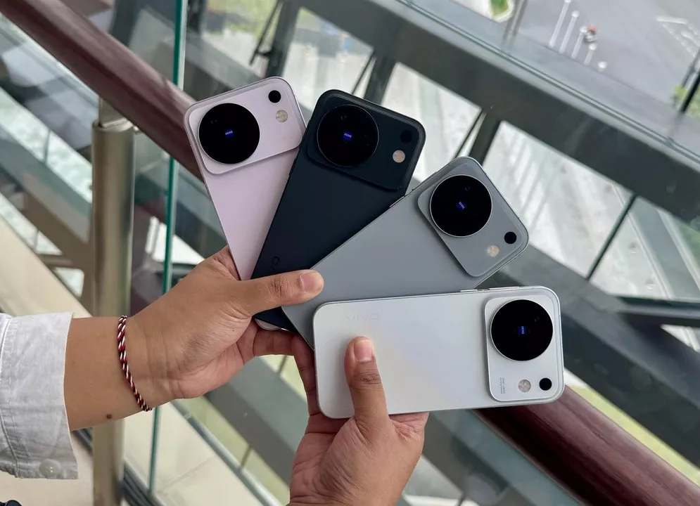 Seseorang memegang empat unit Vivo X500 Series dalam varian warna ungu, hitam, abu-abu, dan putih di dekat balkon.
