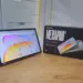 Wujud asli unit Tecno Megapad SE 2 menyala di samping kotak kemasan resminya di atas meja kayu.