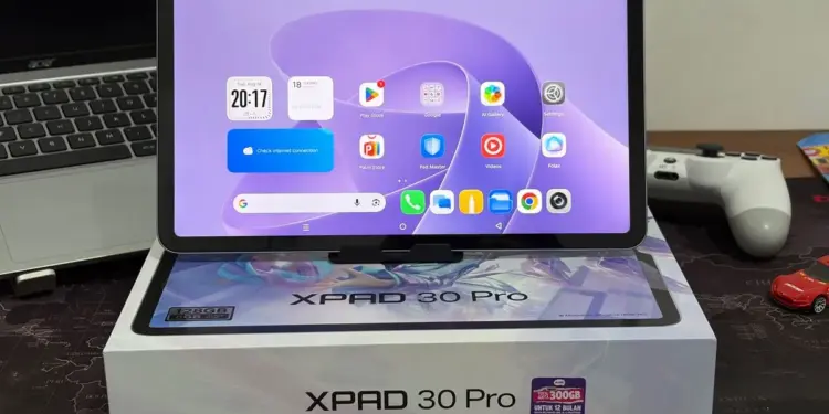 Tablet Infinix XPAD 30 Pro dengan layar menyala menampilkan antarmuka Android, diletakkan di atas kotak kemasan resminya.