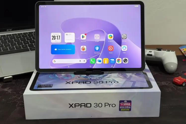 Tablet Infinix XPAD 30 Pro dengan layar menyala menampilkan antarmuka Android, diletakkan di atas kotak kemasan resminya.