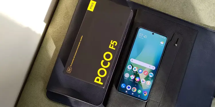 HP Xiaomi RAM 8 GB dengan layar menyala bersanding dengan boks penjualan bertuliskan POCO F5 5G.