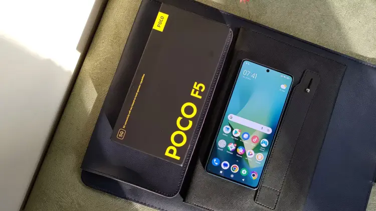 HP Xiaomi RAM 8 GB dengan layar menyala bersanding dengan boks penjualan bertuliskan POCO F5 5G.