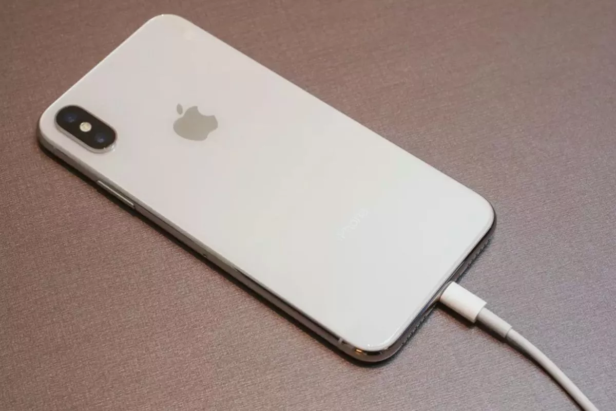 Perangkat iPhone warna putih yang sedang diisi daya akibat isu iPhone boros baterai setelah update iOS.
