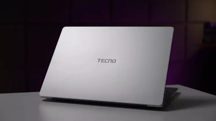 Tampilan cover belakang laptop TECNO berwarna silver minimalis di atas meja.
