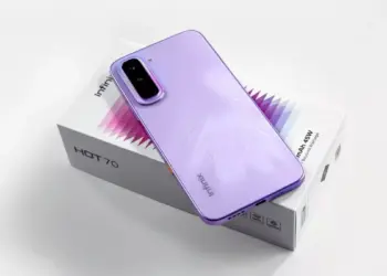 Smartphone Infinix Hot 70 warna ungu diletakkan di atas kotak kemasan produk.