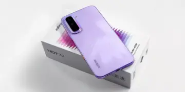 Smartphone Infinix Hot 70 warna ungu diletakkan di atas kotak kemasan produk.