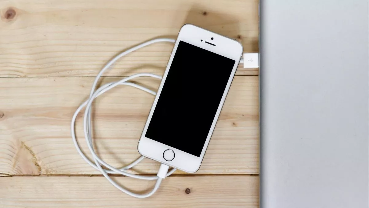 iPhone putih terhubung kabel USB ke laptop saat menangani masalah iPhone boros baterai.