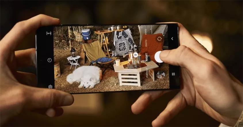 Seseorang mengambil foto anjing di area kamping malam hari menggunakan kamera smartphone